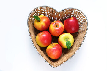 Red apples in straw basket made in the shape of heart on white background. Religious holidays concept - Jewish New Year or Apple spas. 