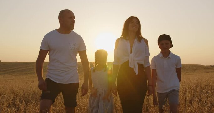 A family with children having fun and walking in a field at sunset