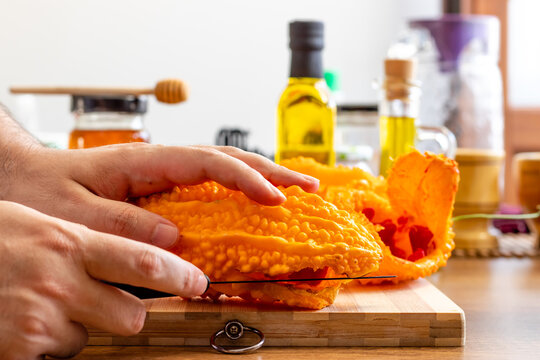 Hands cutting a Momordica charantia in the kitchen - Bitter Melon- balsam pear. Karela. Kudret Nari - Potency Pomegranate.