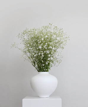 White flower bouquet in white vase on gray interior. Minimalist still life. Light and shadow nature vertical background.