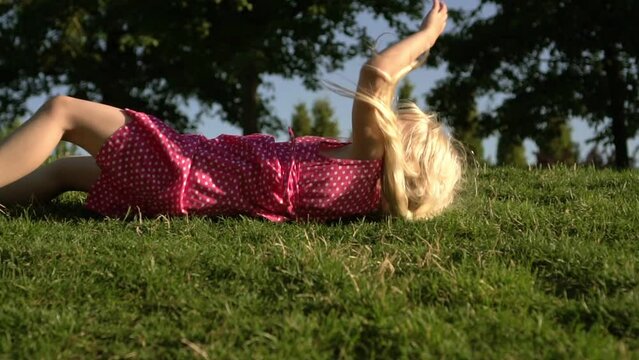 child rolls down the hill on the grass in the park. Happy little girl playing on the grass outdoors in summer.