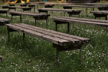View to old outdoor wooden bench rows in blooming meadow.