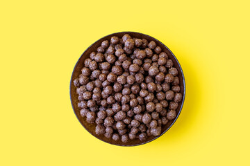 Chocolate corn flakes in a bowl on a yellow isolated background in the center of the image. Flakes with chocolate flavor, close-up top view. American-style energy carbohydrate breakfast