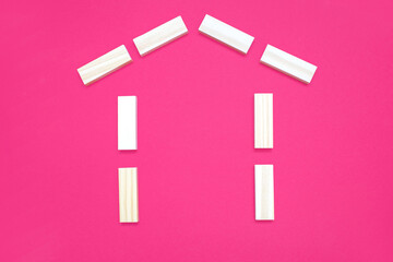 House shape from wooden rectangles on a pink background. The concept of building or buying your own...