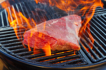 Raw BBQ wagyu sirloin cap of rump beef steak grilled as close-up on a charcoal grill with fire and...