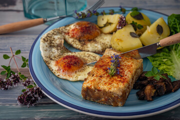 Fried tofu and eggs with lettuce and potatoes on blue circle dish and old table