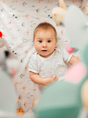 A small child lies in the shelter and looks at the toys above the bed