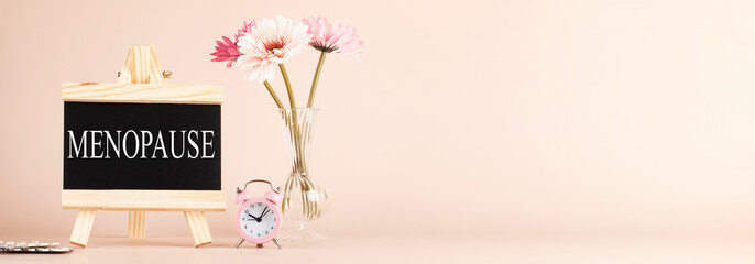 menopause word written on black board, flowers, clock and pills on beige background. women health...