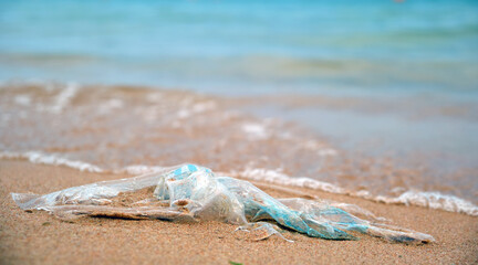 Fototapeta na wymiar Left behind plastic bag garbage on sandy beach. Empty used dirty litter on sea shore. Environmental pollution. Ecological problem