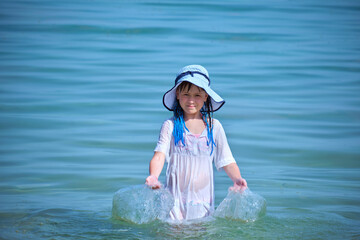 Little child girl in wet white dress and big hat playing alone in sea water enjoying summer vacations