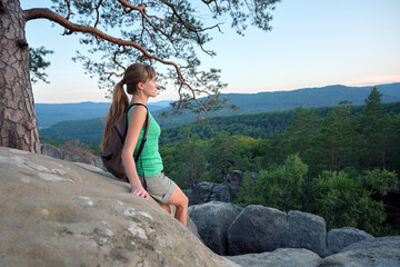 Young woman hiker standing alone with outstretched arms on mountain footpath enjoying view of evening nature on wilderness trail. Active way of life concept