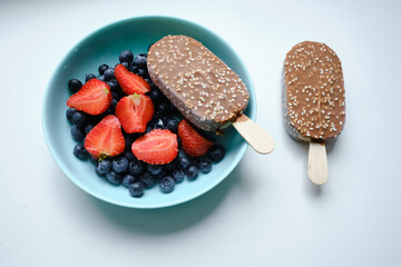 Strawberries, blueberries and chocolate ice cream in blue plates on a light background. Natural ice cream close-up. Fresh organic berries and fruits. Traditional milk product
