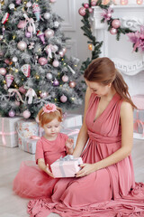 Mother and daughter in soft pink dresses near the decorated Christmas tree.