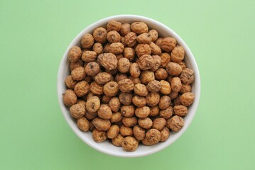 Chufa, tigernut, earth almond on ceramic bowl on green background. Healthy organic food concept. Tiger nut for flour, milk, traditional typical homemade cold fresh drink horchata from Valencia Spain