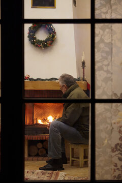 elderly man sitting in front of fireplace. View through window