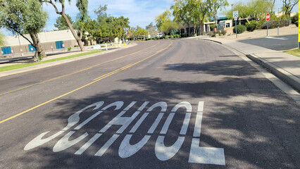 A single word school warning white sign painted on gray asphalt surface of the city road for drivers to be aware of special crossing ahead, Phoenix, AZ