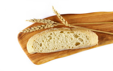 Bread slice with wheat ears on cutting board isolated on white