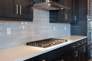 Modern kitchen details of smooth counter, gas stove, tile backsplash, and black cabinetry.