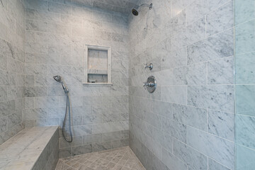 Luxury walk in shower with gray and white marble walls, bench, and flooring with chrome finishes. 