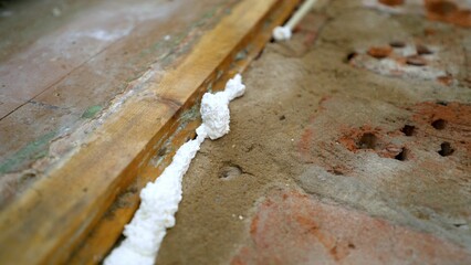 Man worker fills crack between wall and cement floor with mounting foam in room. A worker uses foam...