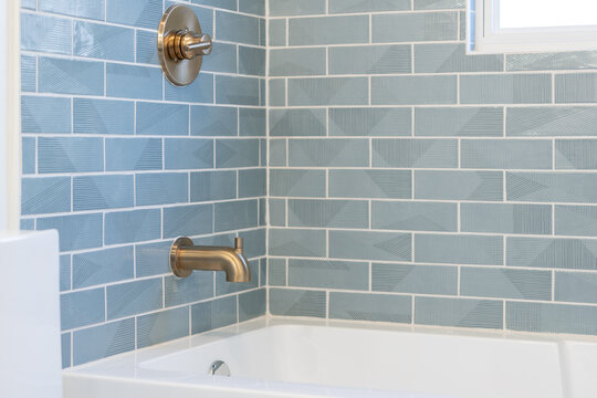 Light blue tile patterned bath tub tile with gold faucet and handle.