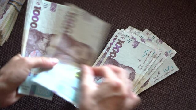 Female hans counting ukraininan hryvna  banknotes nominated 1000.