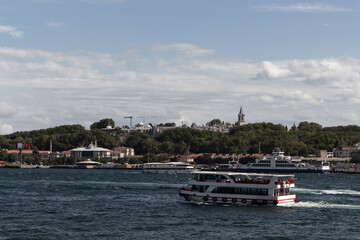 View of Bosphorus tour boats passing in front of Topkapi Palace in Istanbul. It is a sunny summer day.