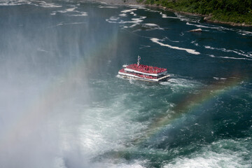 Yacht with many tourist on running into storm misty in splash white water with rainbow across the water background, Niagara Falls USA.