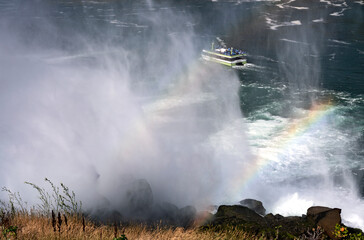 Misty water splash over big river with rainbow on the water while big boat on travel