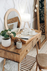 Wooden boudoir table with vintage chair. Full length mirror with wooden frame. Flowers in pots indoors. Wooden floor. Scandinavian style handmade wooden furniture. Boho style interior. Nobody