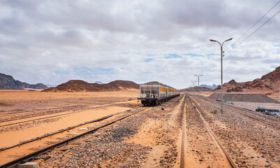 Old unused train at Wadi Rum train station, overcast sky above sandy desert around