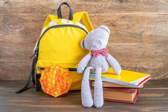 Education background with bear toy, sensory fidget toy, backpack, notebooks on wooden surface.