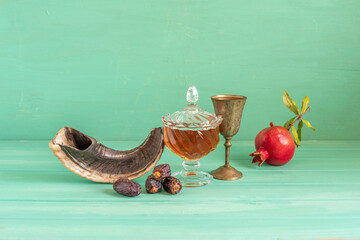 Fresh honey, pomegranate fruit, date fruits, musical horn Shofar, bronze goblet for Jewish holiday Rosh Hashanah on green wooden background.