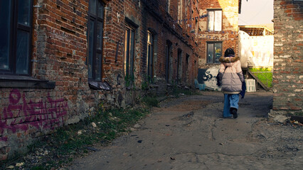 Young hipster woman walks through the streets of the city. Stock footage. View from the back of a young woman walking along narrow streets near brick walls