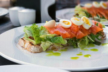 Big tasty sandwich with salmon, quail eggs and greens. Lunch at a restaurant. Proper nutrition.