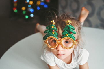 a little serious girl, a child with a grimace in funny New Year, Christmas glasses on the...