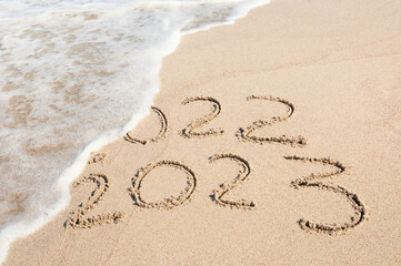Inscription 2022 and 2023 numbers written on sand.  New Year 2023 replace 2022. Concept on the sea beach