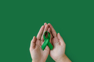 Adult hands holds green ribbon on green background. World lymphoma awareness day. September 15....