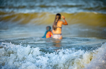 Two sisters in summer swimsuits splash in the sea waves aground on a sunny evening of vacation