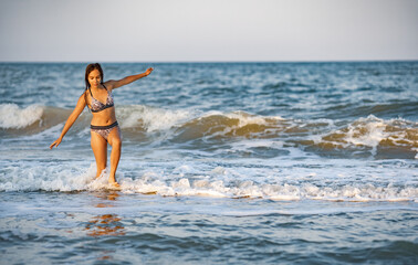 A girl with loose hair walks on the sea with waves and enjoys the sun