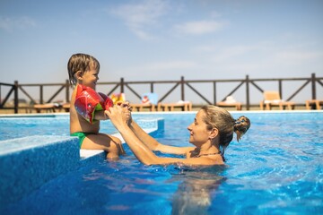 Fototapeta premium Mom plays with her son with oversleeves in the pool in summer