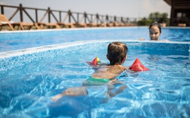 Kid in oversleeves in the pool and playing with his sister on summer vacation
