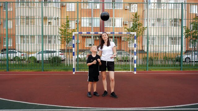 Portrait of a son with his mother standing against the background of a football goal and throwing a soccer ball into the air.