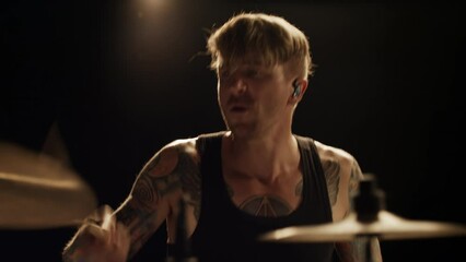 Caucasian rock musician drummer with tattoos aggressively plays drums in a dark room in smoke.