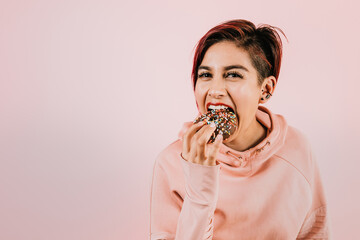 Portrait of young hispanic woman eating donuts on coral pink background in Mexico Latin America