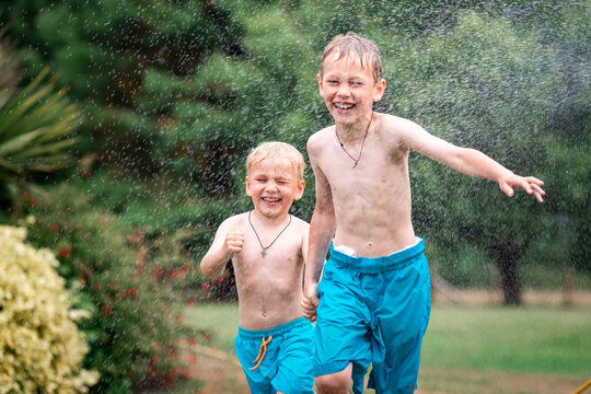 Kids play with water on hot summer day. Children with garden sprinkler. Outdoor fun. Boys run on a field under water drops.