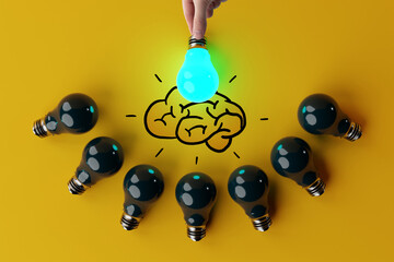 A hand holds a lit light bulb against the background of other extinguished light bulbs and a sketch...
