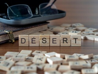 désert mot ou concept représenté par des carreaux de lettres en bois sur une table en bois avec des lunettes et un livre