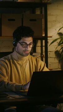 A young man typing on a laptop and talking into a microphone in the office