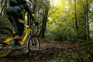 Cyclist in full face helmet on the yellow enduro bicycle fast rides in the mud in a green forest
